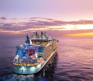 OA, Oasis of the Seas, aerial shot of ship at sea, sunset, dusk, evening, 3/4 aft starboard view, ocean horizon, red, orange, purple colors, AquaTheater and slides at rear of ship, scenic, seascape